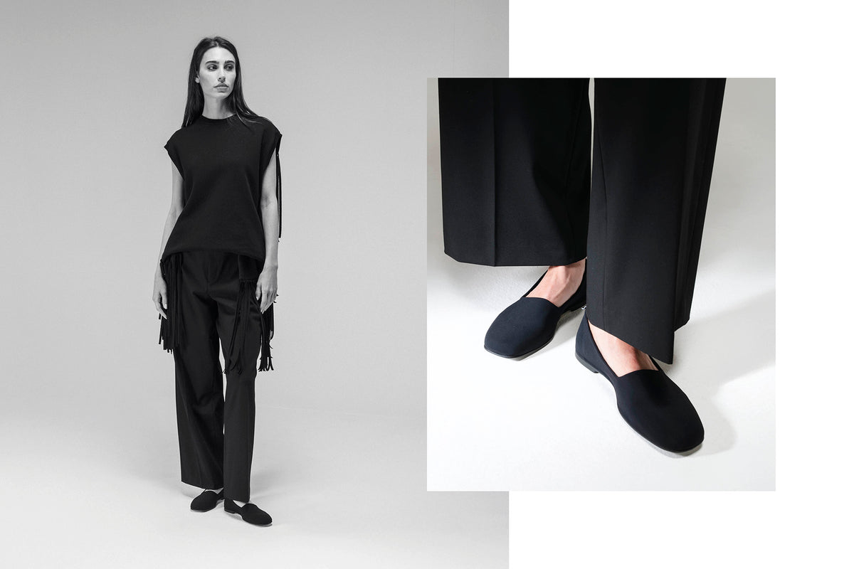 A model wears a black sleeveless top and wide-leg trousers with fringe, paired with black slip-on shoes, shown against a light gray studio background with a close-up inset of the shoes. Style Soffy from the Fall/Winter Collection.